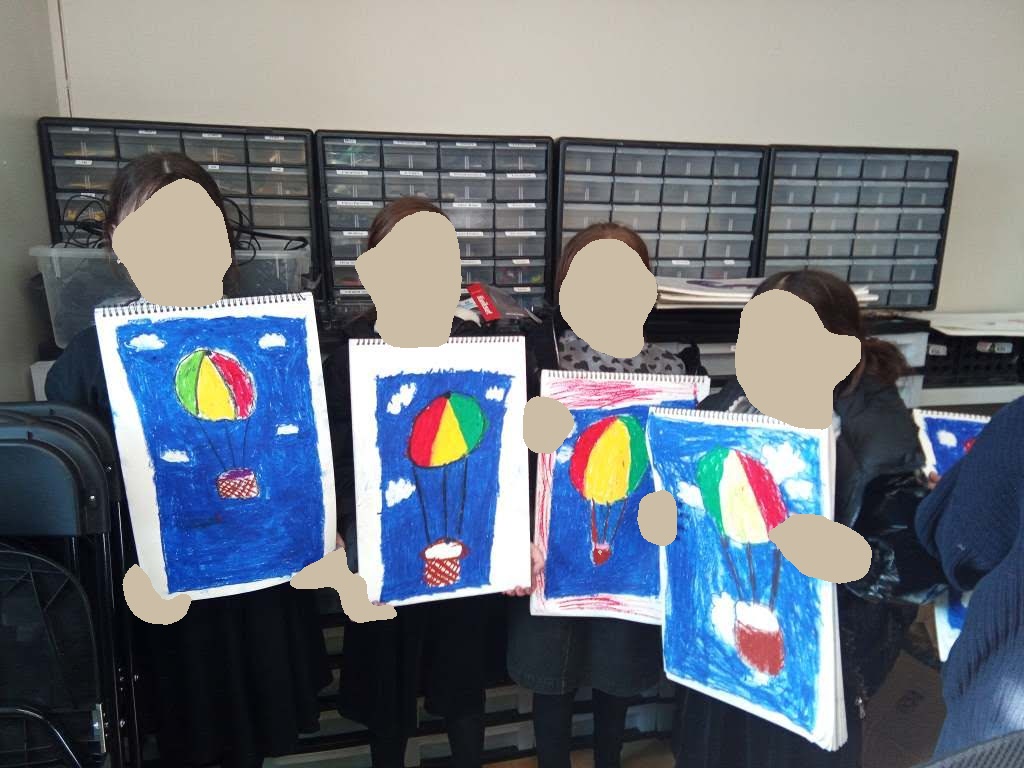 Glitter Girls holding up their hot air balloon paintings in art class